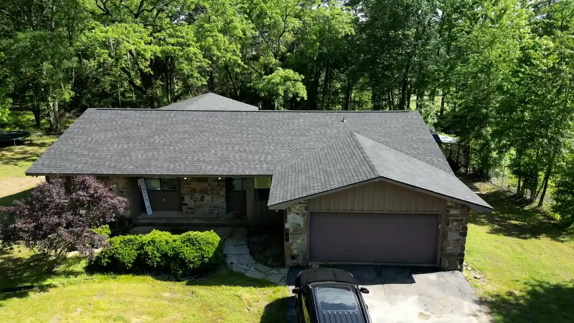 Stone-front hillside home on a heavily wooded lot with a finished shingle roof